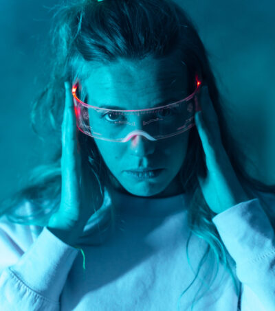 Woman with futuristic glasses gesturing against a blue background, illuminated glasses